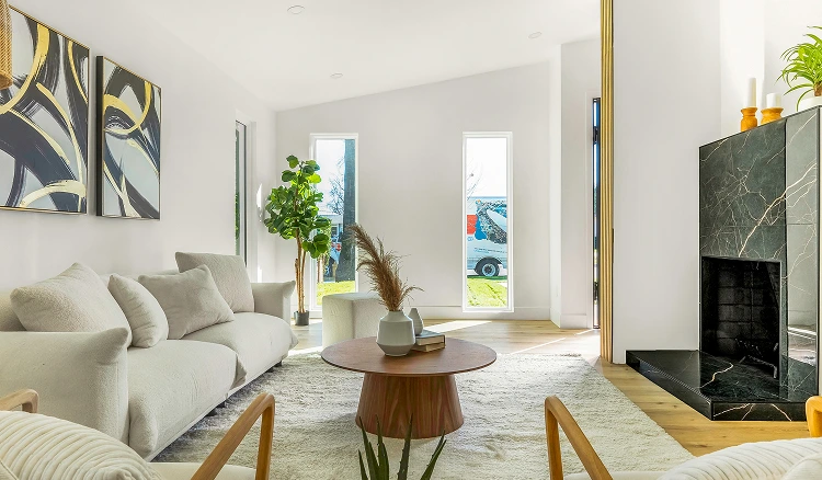 A modern living room with a minimalist design. The room is painted in white with large windows that let in natural light.